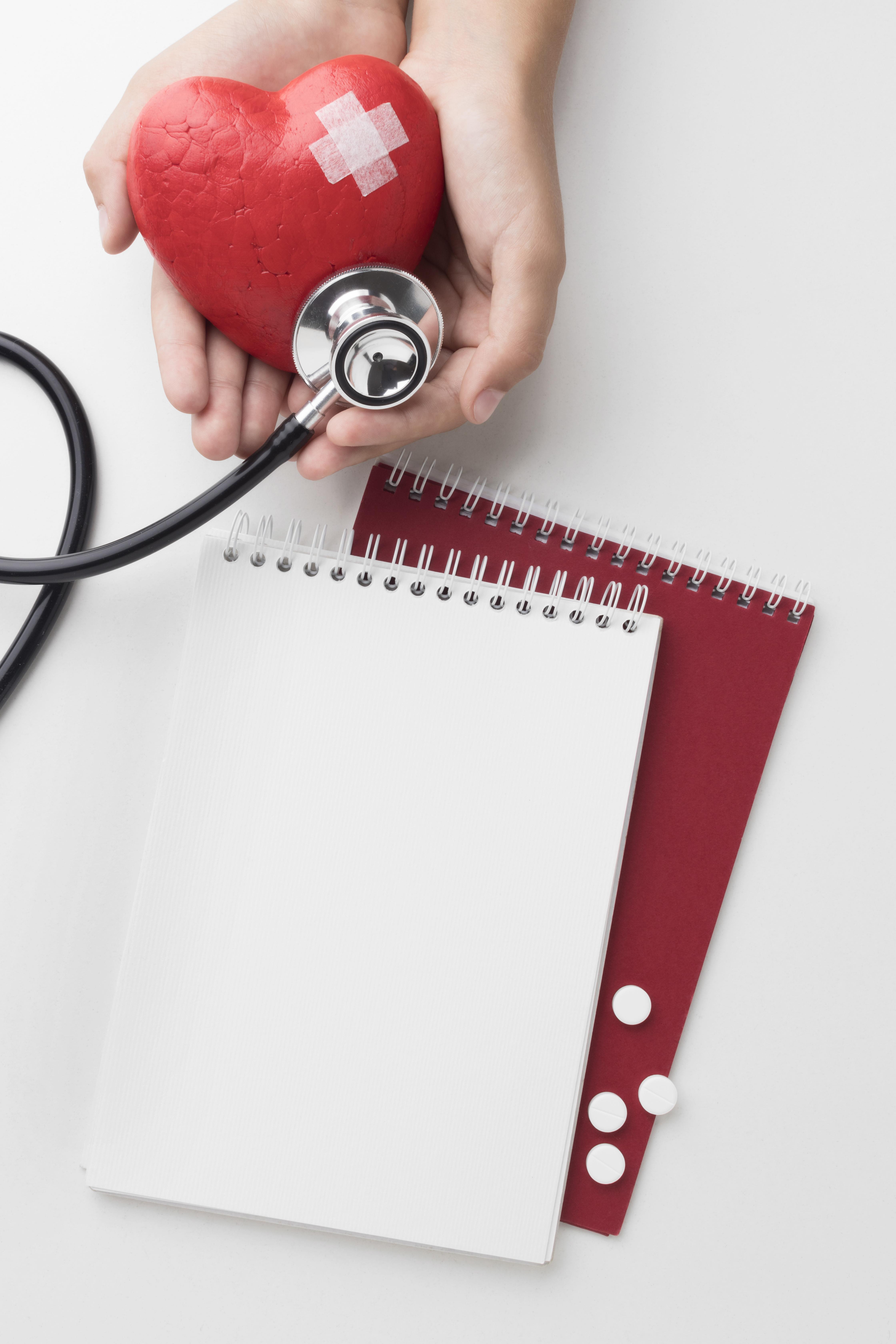 Mãos segurando coração com curativo e estetoscópio, simbolizando prevenção em saúde e redução de absenteísmo nas empresas.