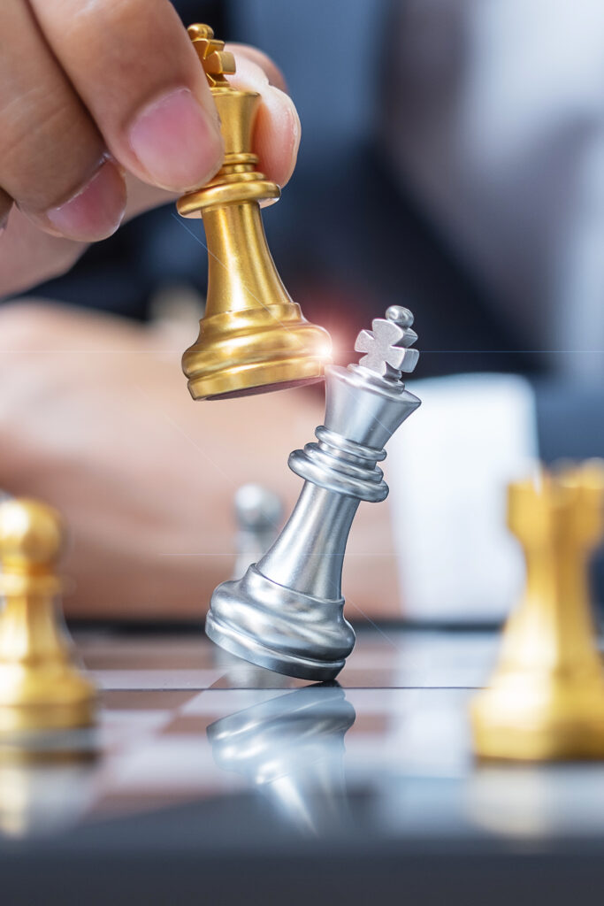 Peça de xadrez dourada derrubando peça prateada, simbolizando competitividade empresarial e estratégia de negócios.