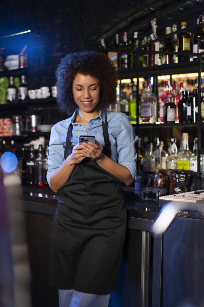 Empreendedora MEI atendendo clientes em bar e utilizando o celular para acessar telemedicina pelo plano de saúde em Juiz de Fora.